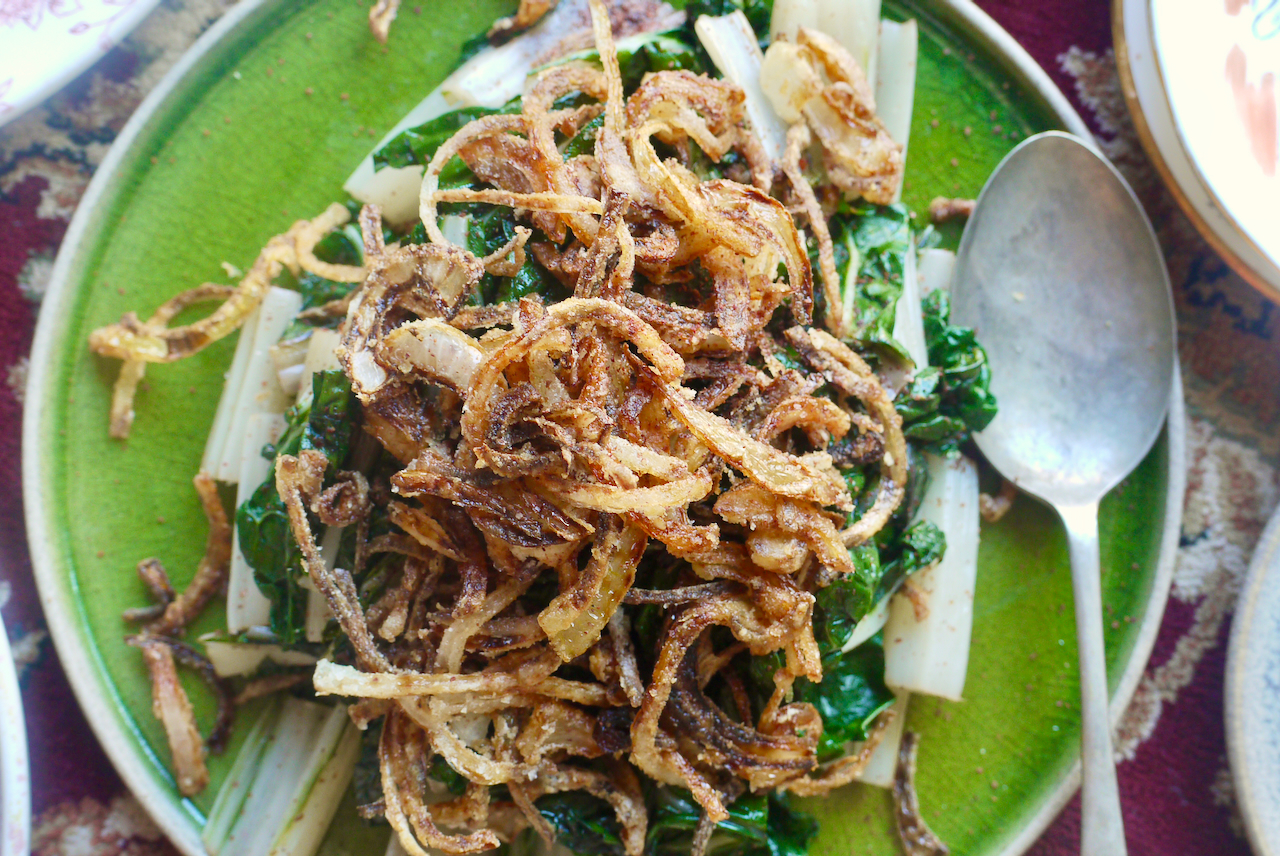 Close up of fried onions on top of silverbeet on a green plate