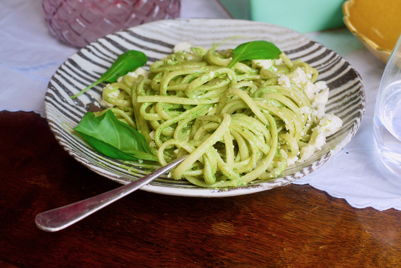 A black and white plate of tallarines verdes with a fork and basil leaves on top