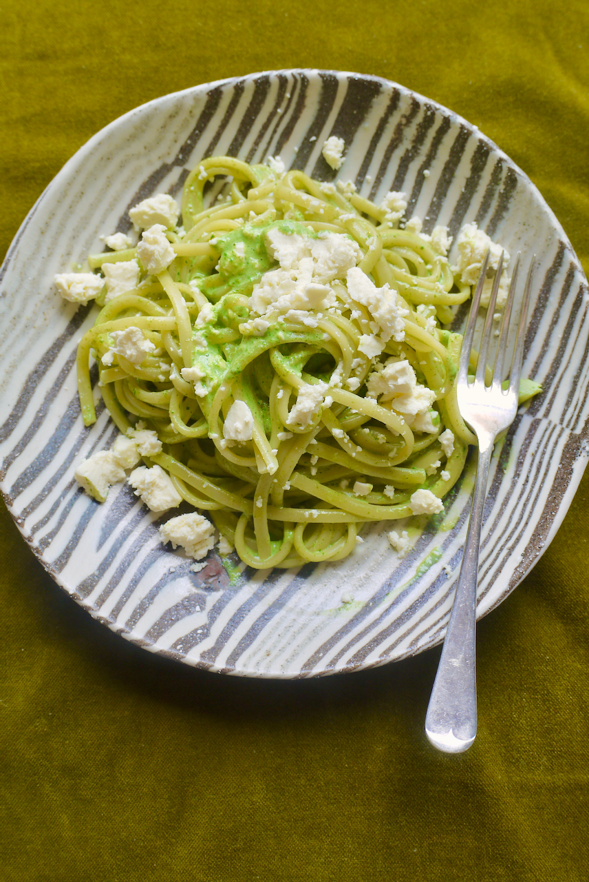 Tallarines verdes on a black and white striped plate with a fork on a green velvet backdrop