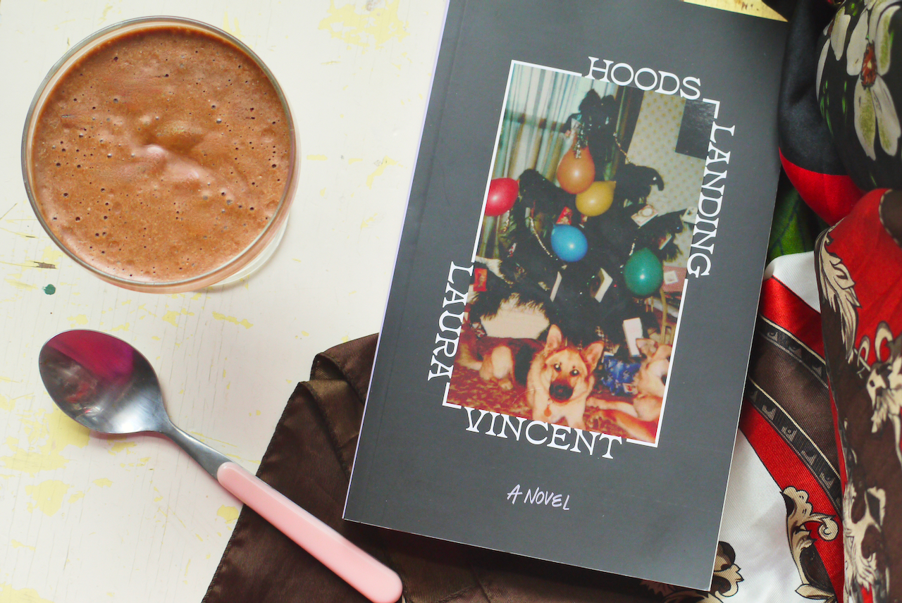 A copy of Hoods Landing, a pink teaspoon, and a coupe glass of chocolate mousse