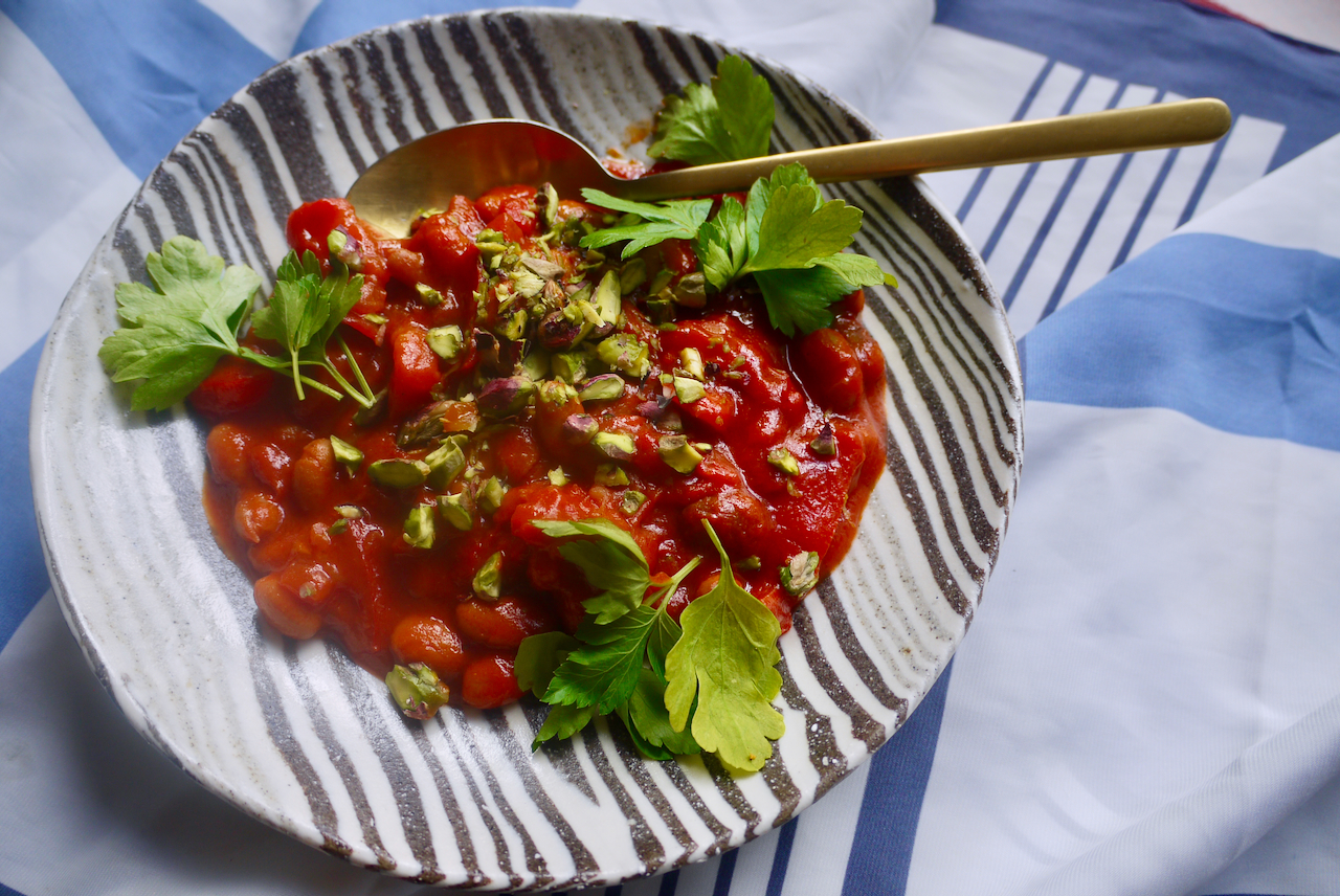 Triple tomato beans and a gold spoon on a black and white striped plate, sitting on a blue and white cloth