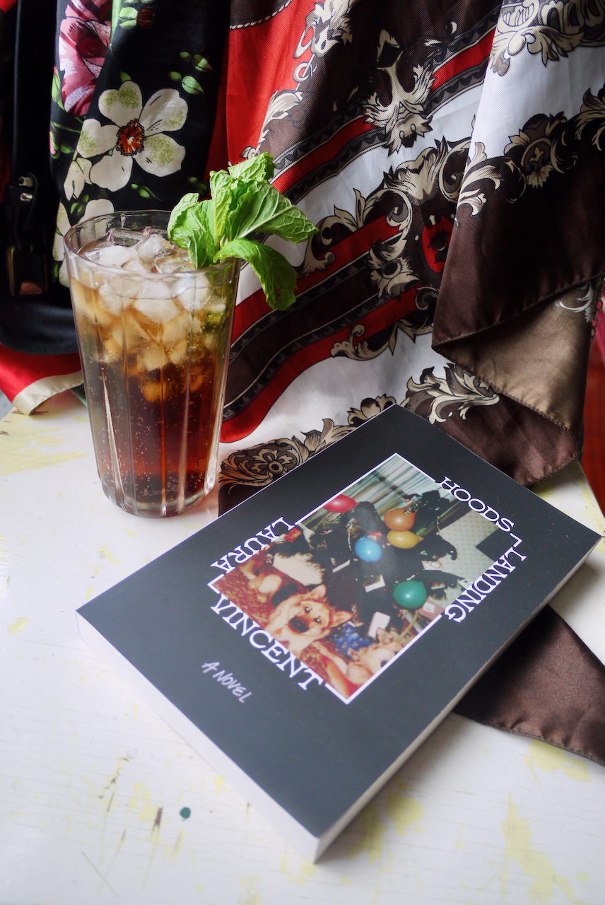 A cocktail in a tall glass with a mint garnish next to a copy of Hoods Landing