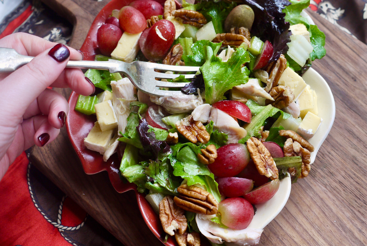 A hand with red nails using a fork to pick up salad from a leaf-shaped plate