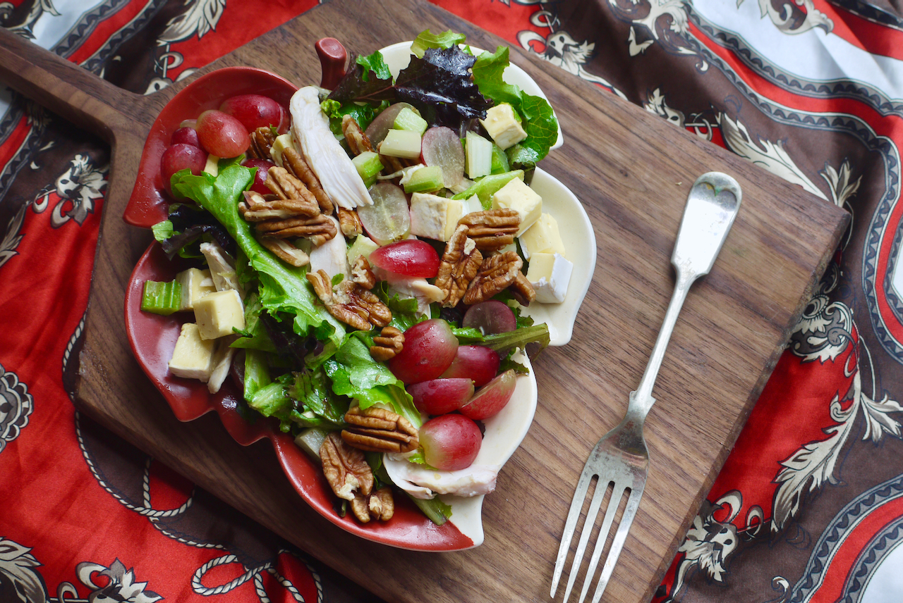 A top-down shot of a leaf-shaped bowl of salad with a fork on a dark wooden board