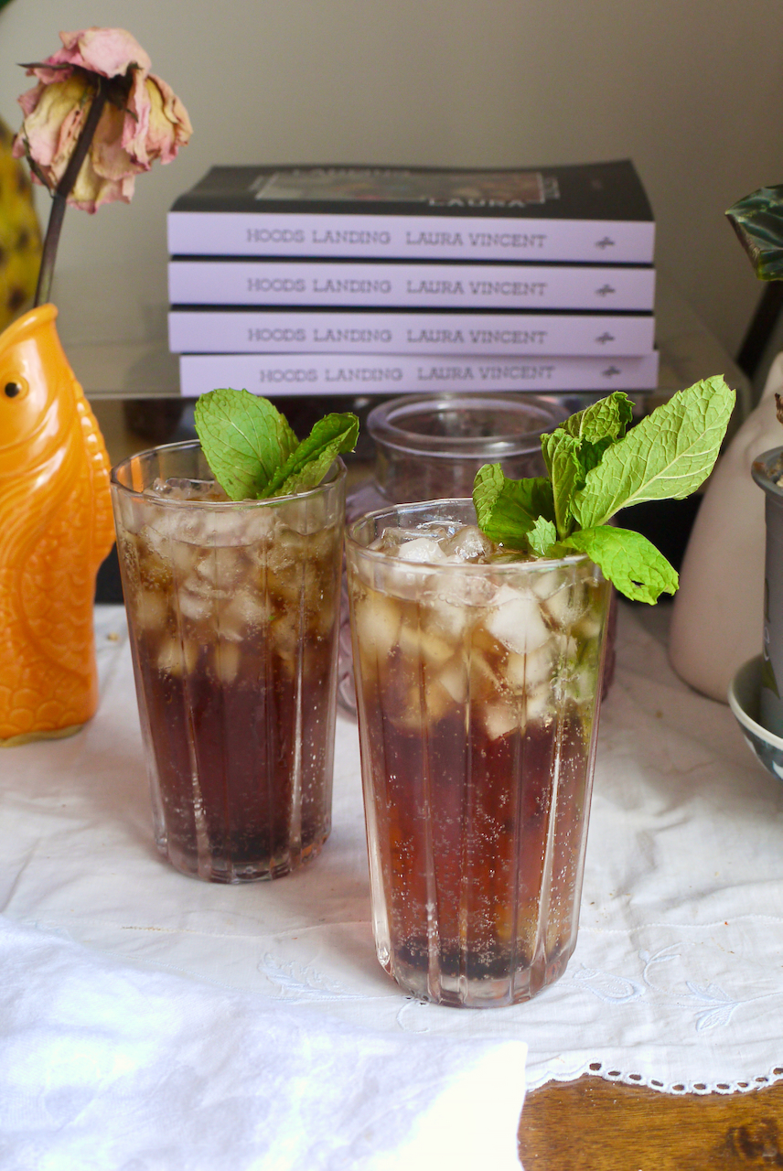 Two cocktails in tall glasses with mint garnish and four books in the background