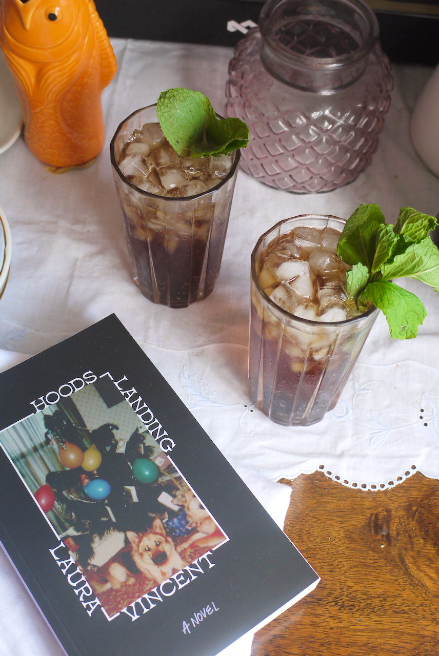 Two cocktails next to a copy of Hoods Landing on a white tablecloth