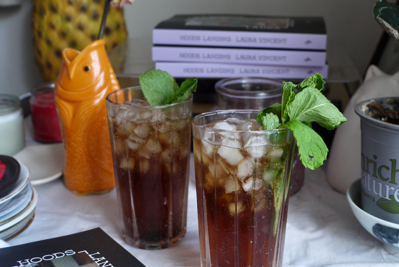 Two mint-garnished cocktails with a goldfish vase and novels behind them