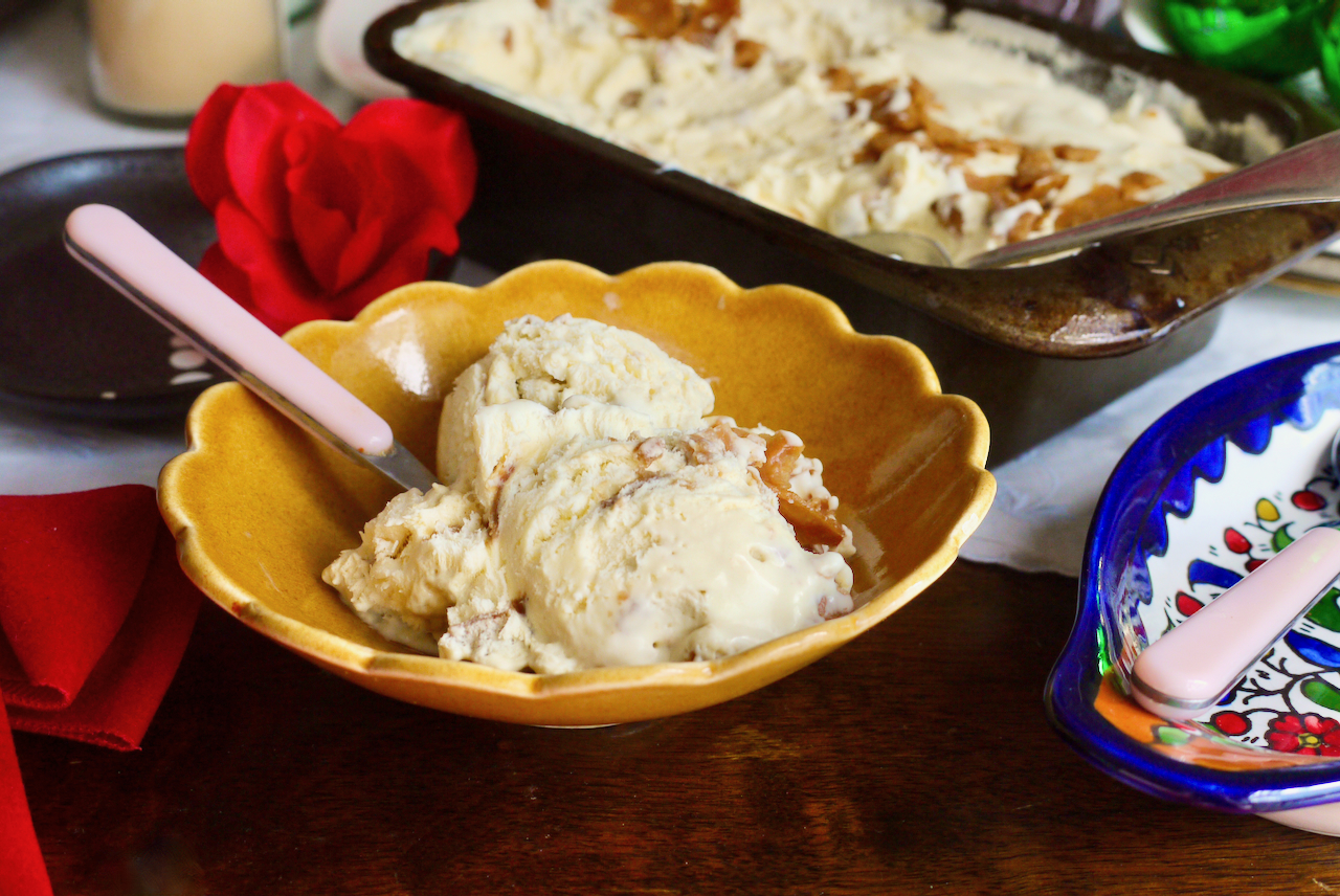 A brown scalloped bowl of ice cream with a pink spoon and a red fabric rose in the background