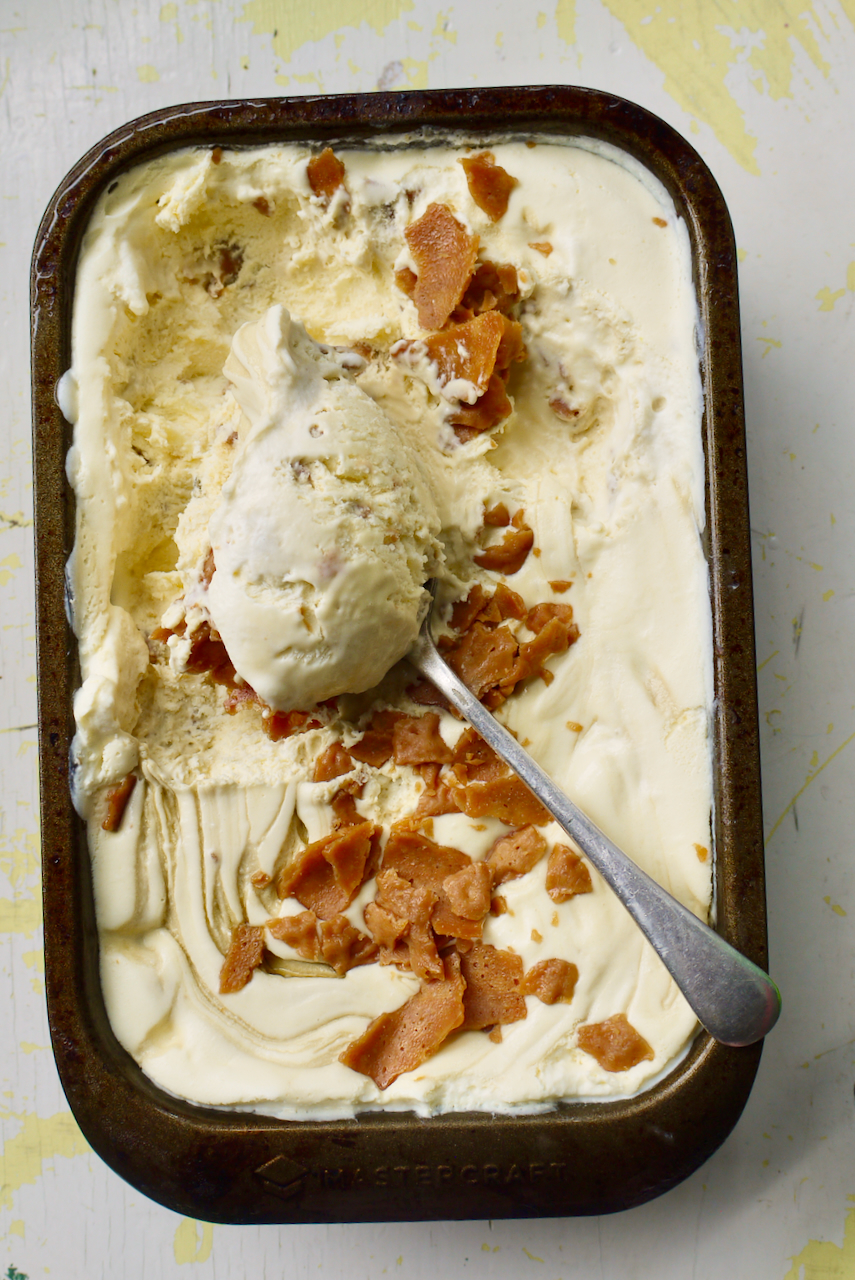 A tin of brandy snap ice cream with a spoonful of ice cream resting on it, against a white background