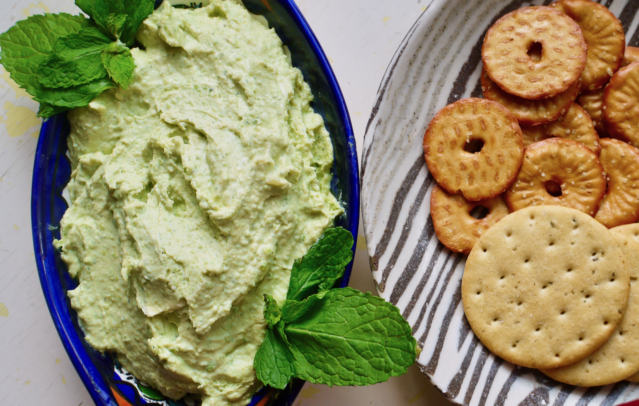A plate of crackers next to a blue dish of pea, mint and feta dip
