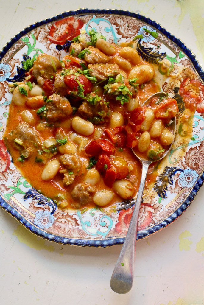 A blue and red patterned plate of sausages and beans on a white painted background