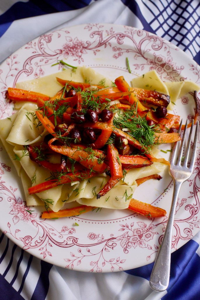 a fork resting on a pink and white plate of pappardelle with roasted carrots