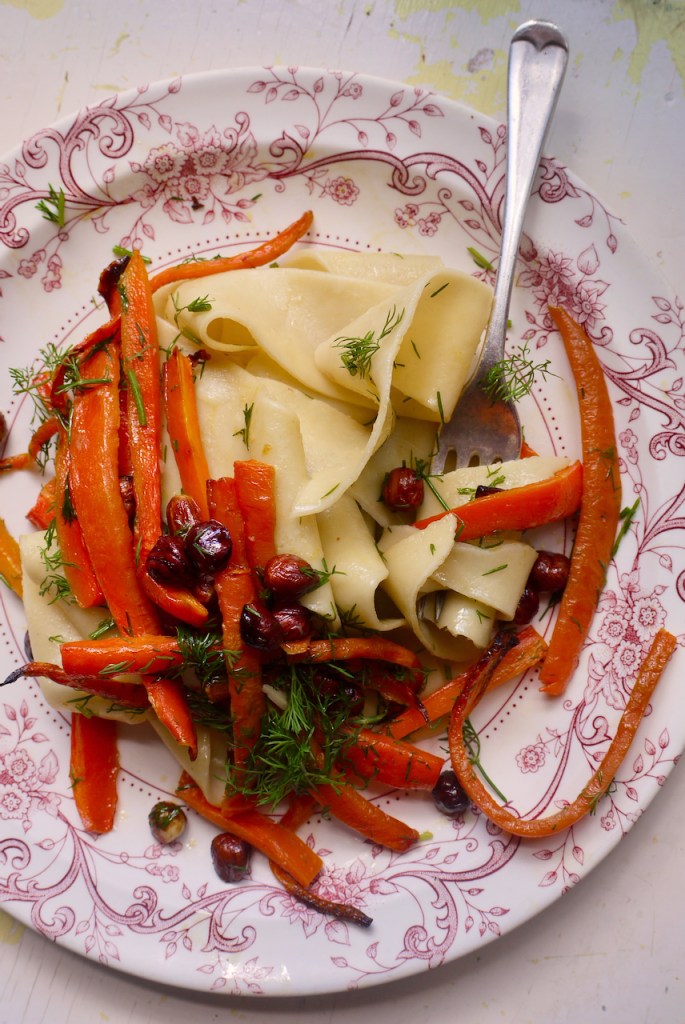 a fork resting on a pink and white plate of pappardelle with roasted carrots