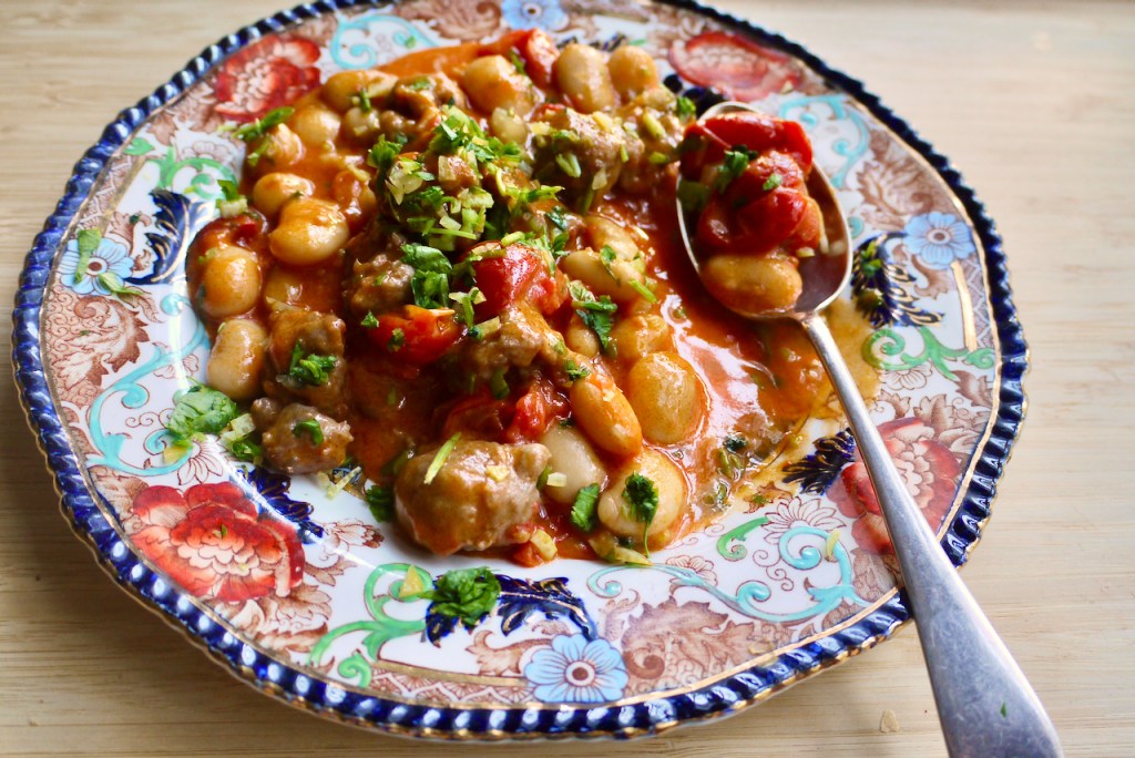 A spoon resting on a blue and red plate of sausages and beans on a wooden table