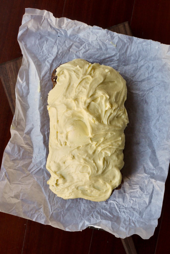 A top down view of an iced loaf cake on a crumpled piece of baking paper