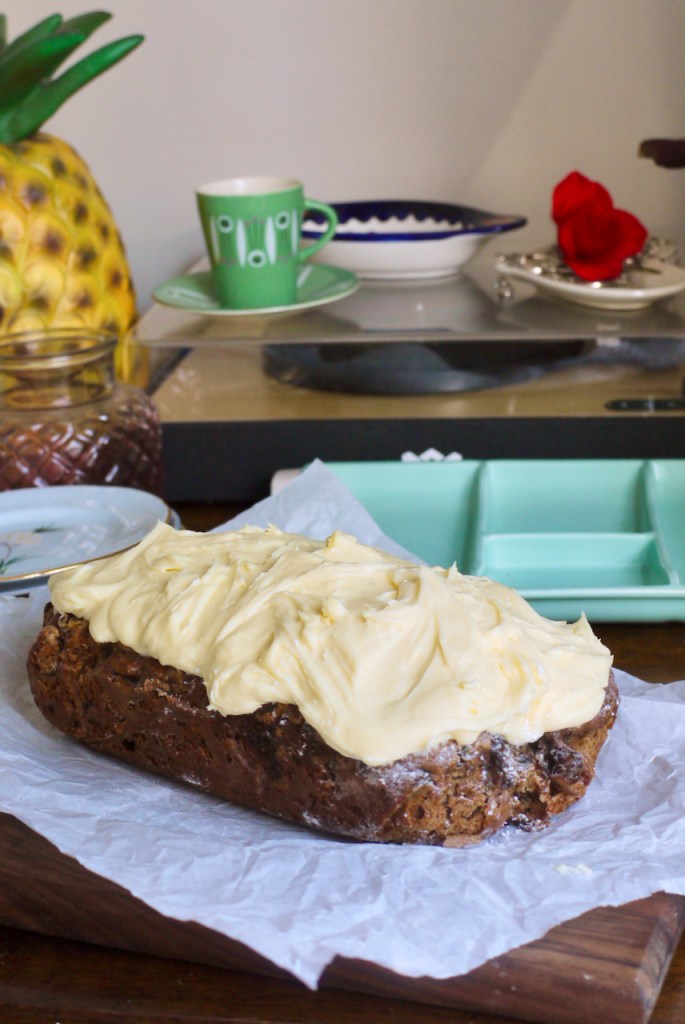 An iced loaf cake on a table in front of a green cup and saucer