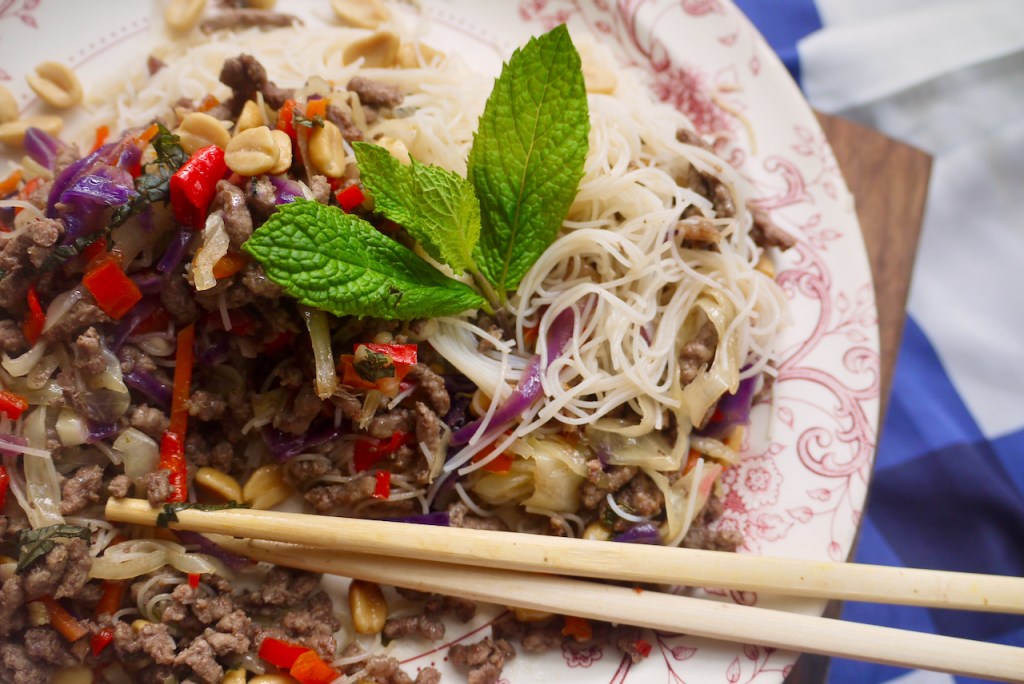 A close up of chopsticks and a mint sprig on a plate of beef and noodles