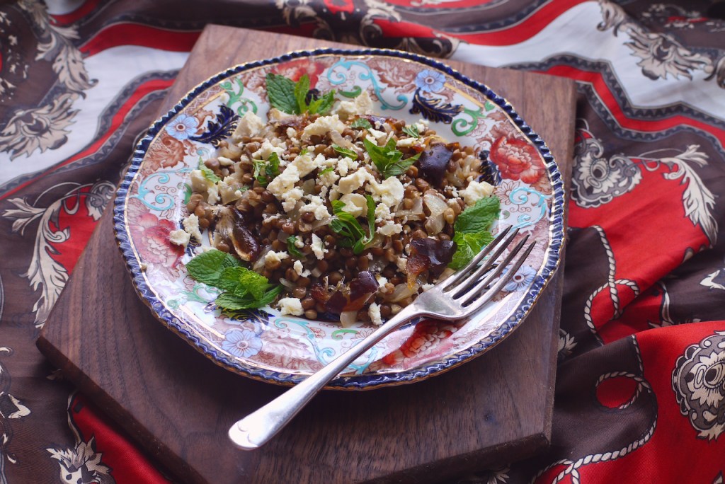 A fork resting on a plate of lentil salad on a wooden board on red and brown fabric
