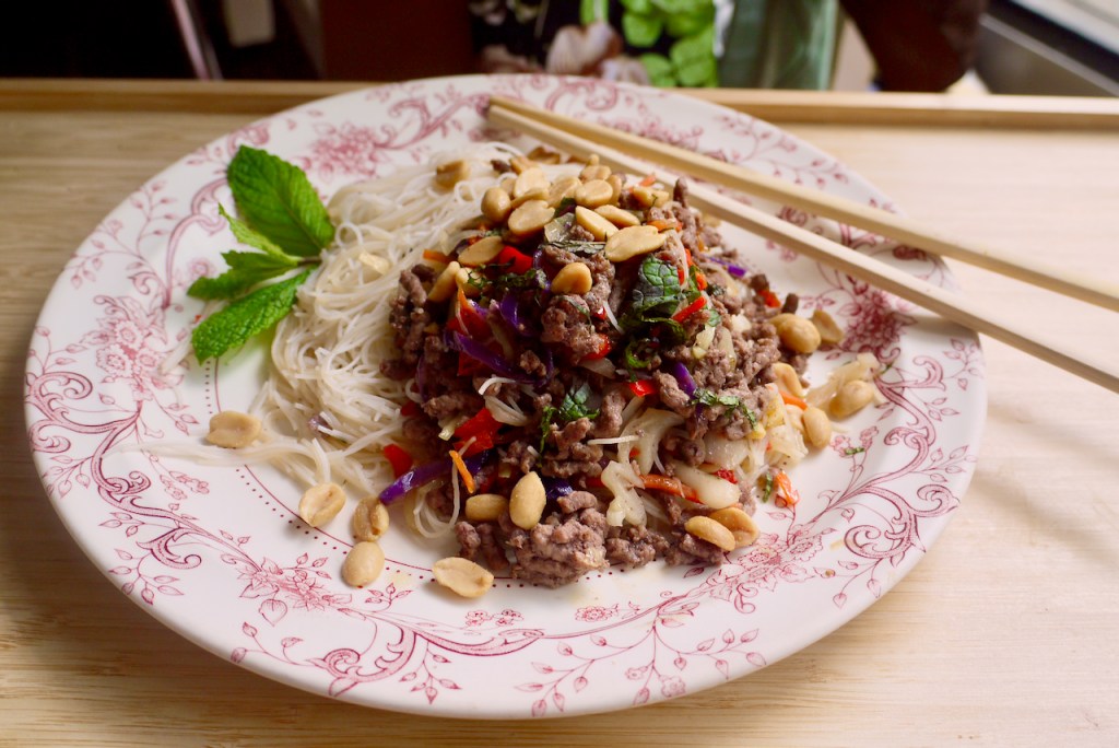 A pink and white plate of beef and noodles with chopsticks on a wooden table
