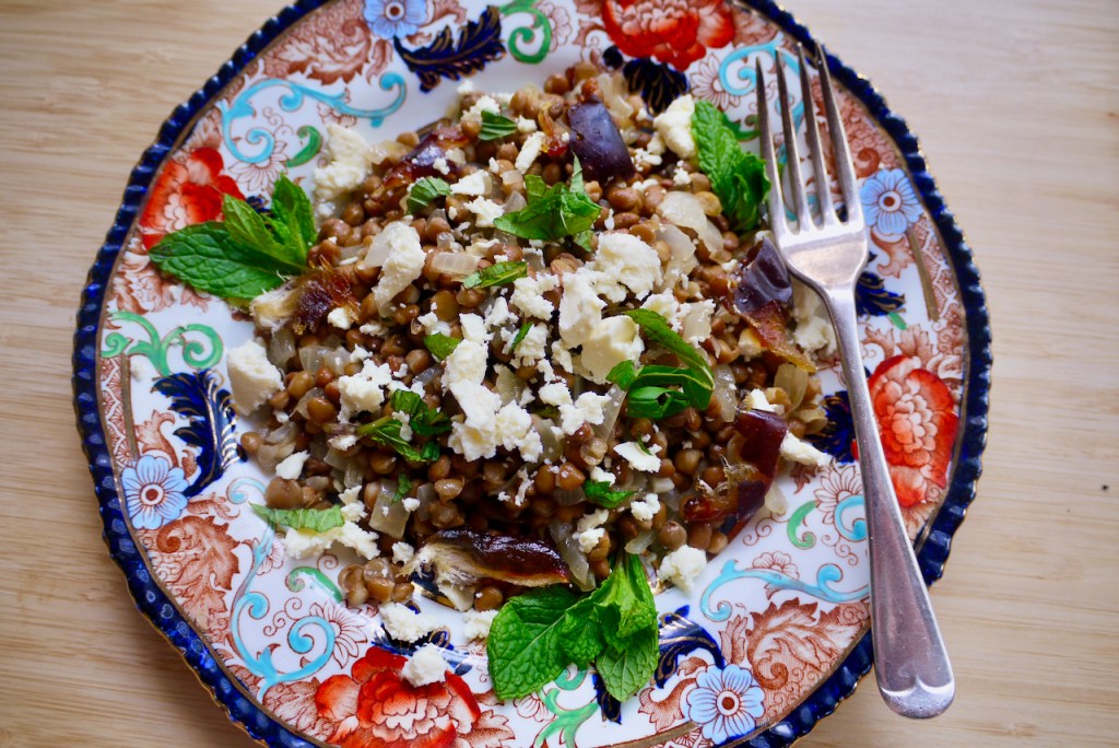 A red and blue plate of lentil salad with mint leaves and a fork on a wooden table
