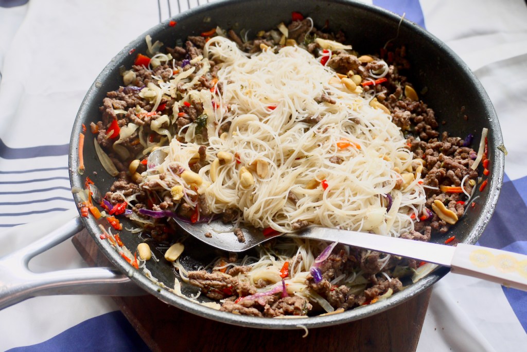 A serving spoon in a pan of beef and noodles on a blue and white cloth