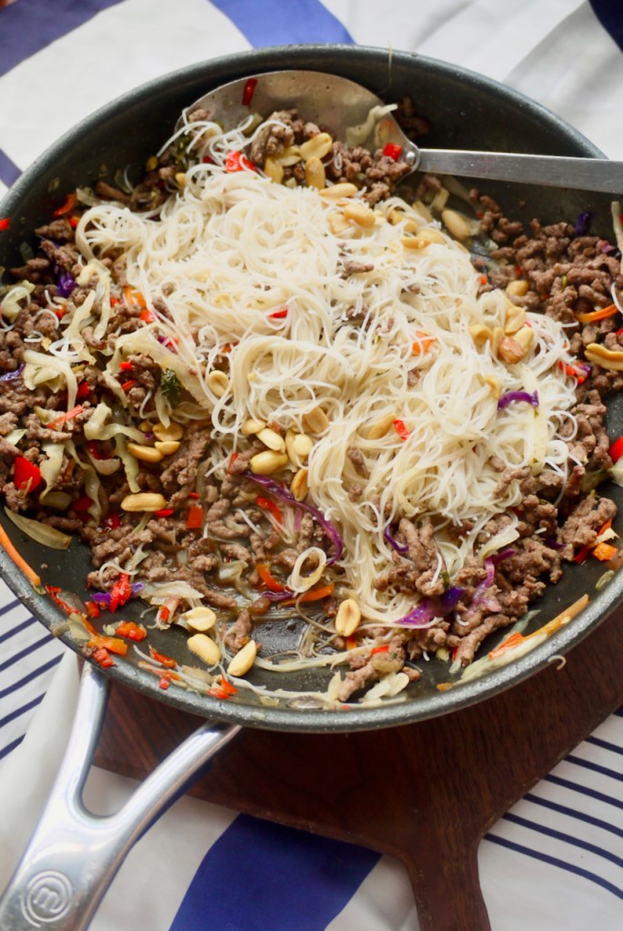 A spoon resting in a pan of beef and noodles on a blue and white cloth