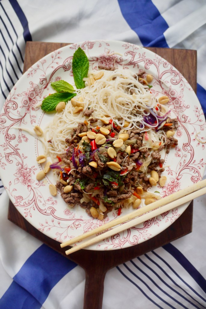 Chopsticks and a mint sprig on a pink and white plate of beef and noodles