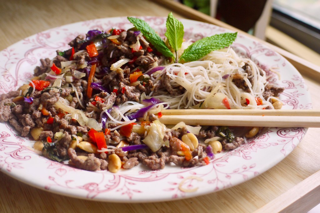 Chopsticks resting on a plate of beef and noodles on a wooden table