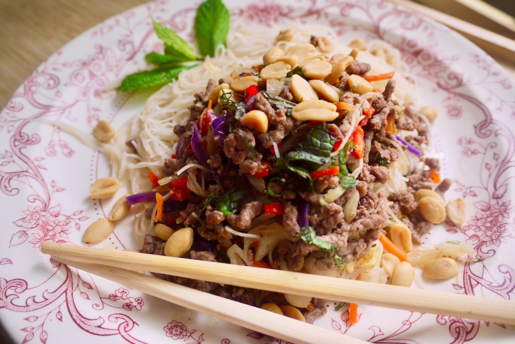 Chopsticks resting on a plate of beef and noodles