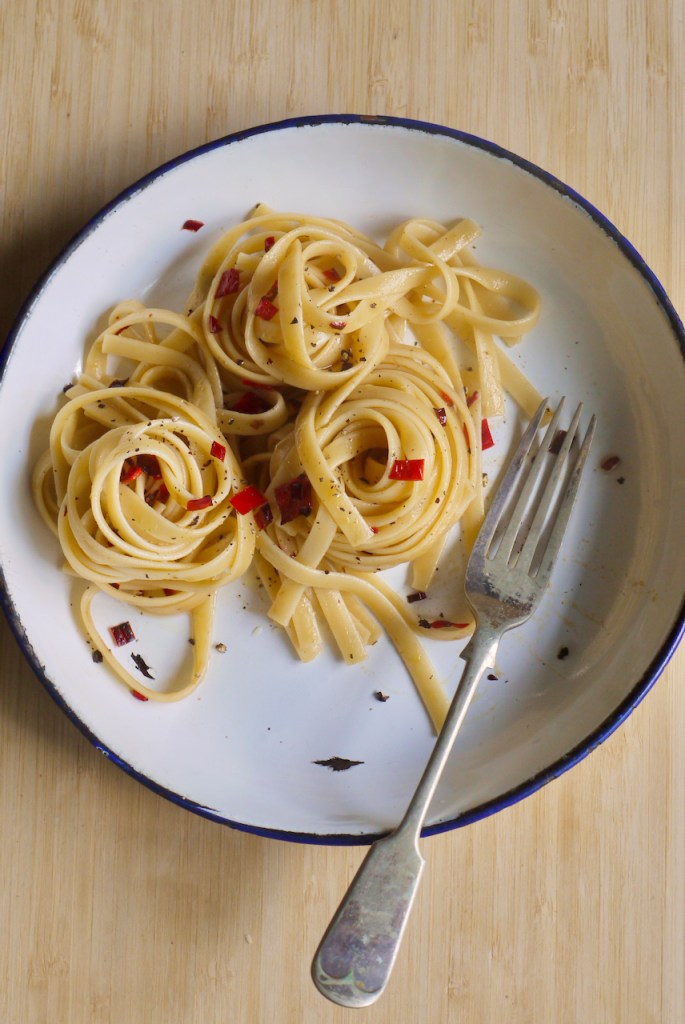 A fork resting in a white plate of pasta and chilli
