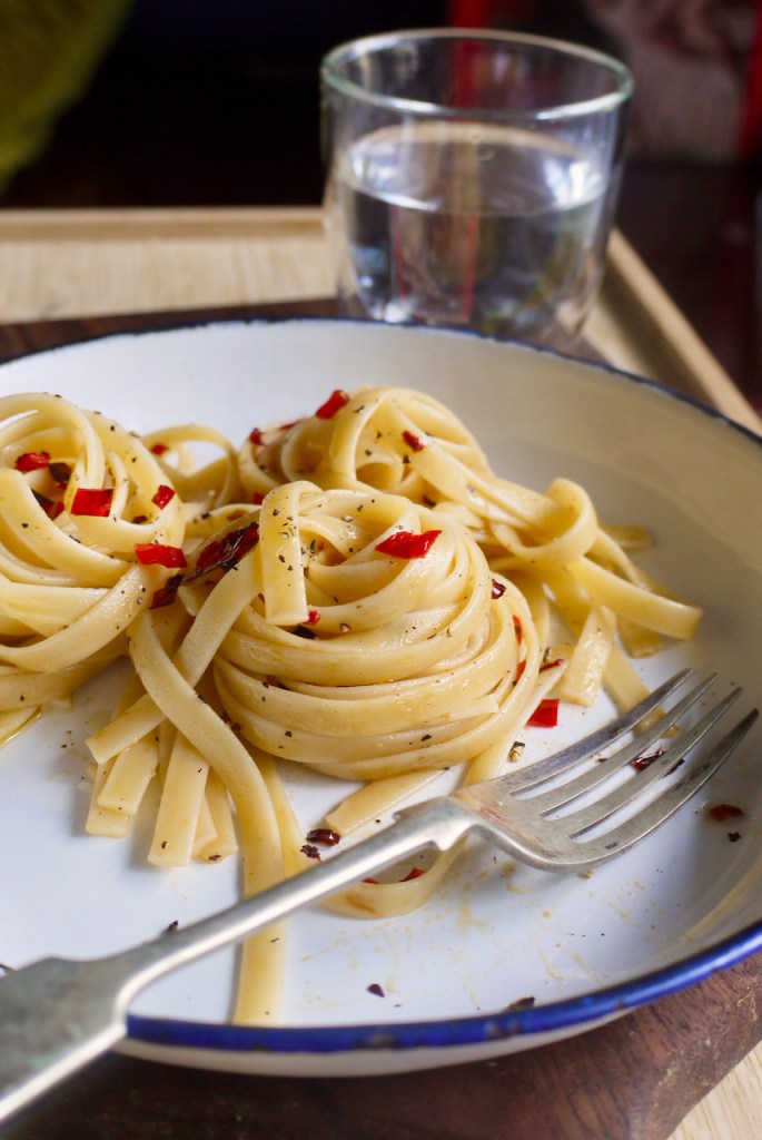 A white plate of chilli pasta with a fork and a glass of water