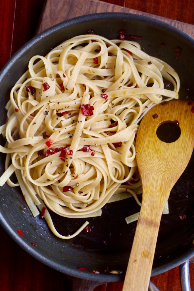 A wooden spoon resting in a saucepan of pasta