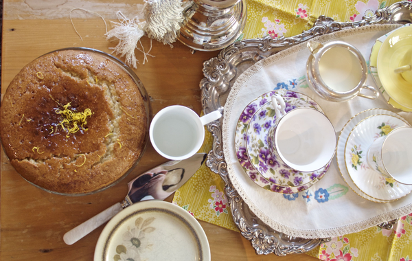 A lemon cake surrounded by cups of tea and plates. This image links to the recipe.