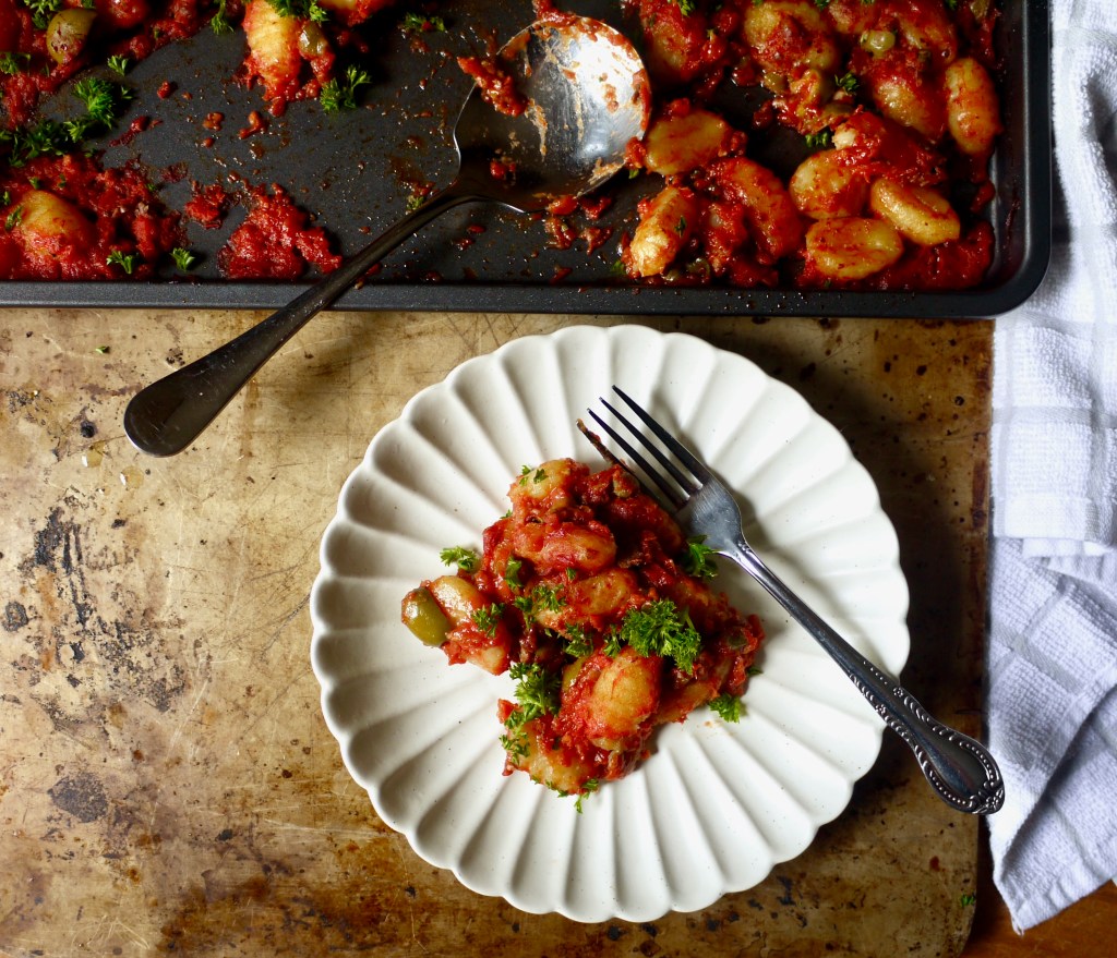 A plate of gnocchi in front of a serving tray of more gnocchi