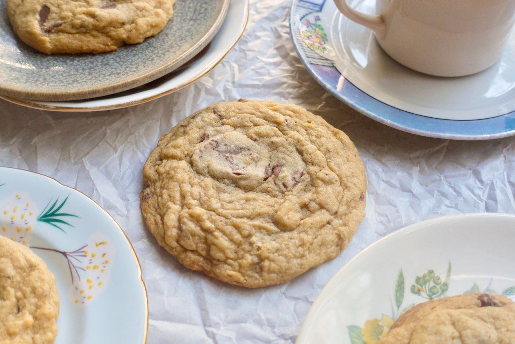 a chocolate chip cookie on a sheet of baking paper surrounded by small plates with more cookies on them