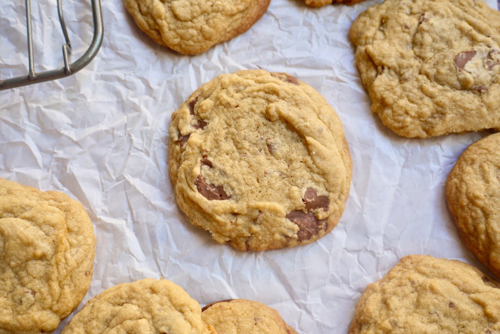 a chocolate chip cookie surrounded by more cookies on a sheet of baking paper