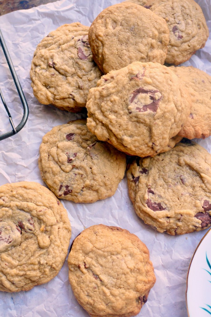 A pile of chocolate chip cookies on a sheet of baking paper next to a cooling rack