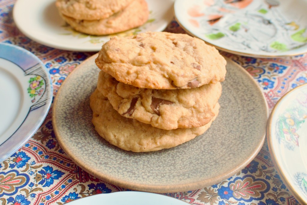 A stack of three cookies on a grey plate, surrounded by more plates