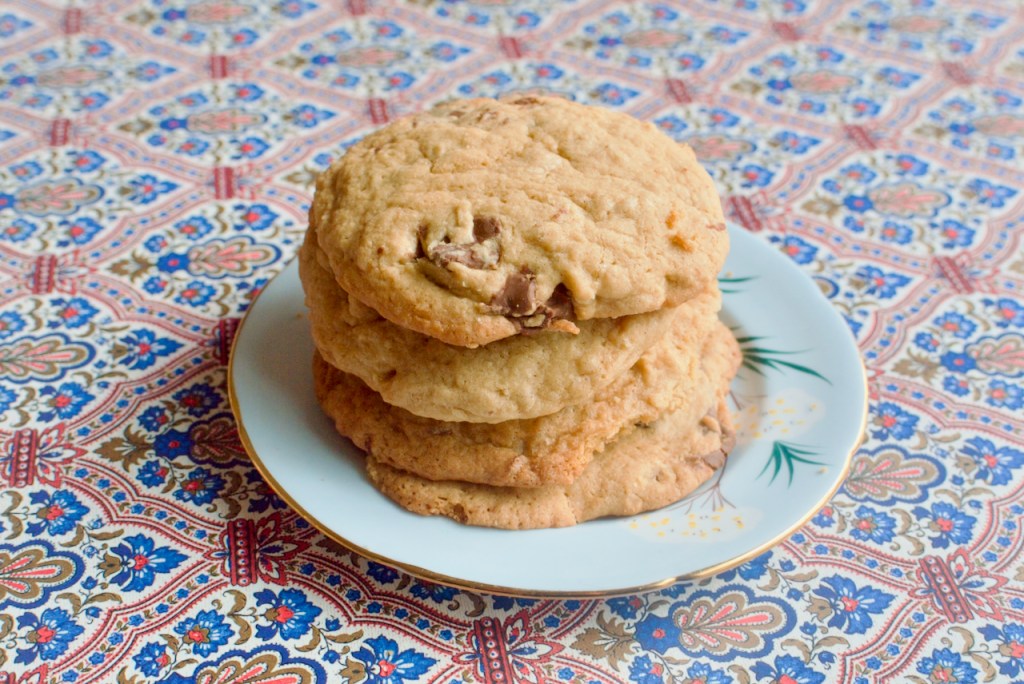 Three chocolate chip cookies stacked on a light blue plate, on a red and blue patterned background