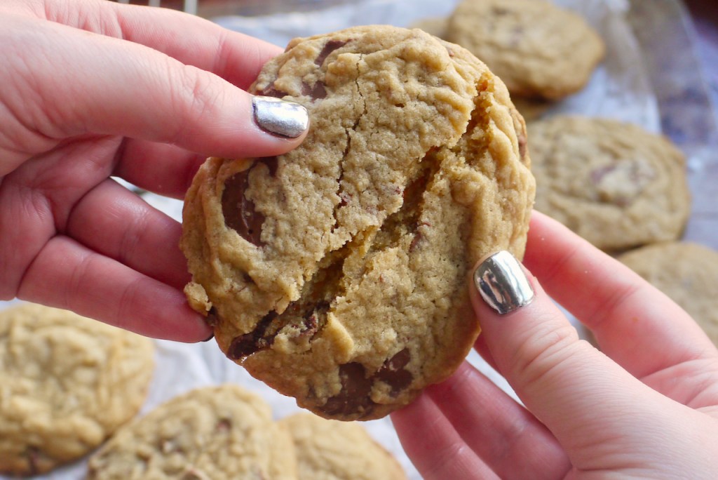 two hands with silver-painted nails breaking a chocolate chip cookie in half