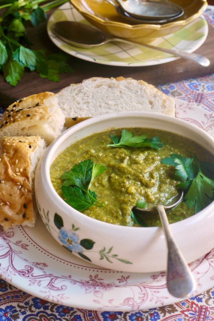 A bowl of soup on a white plate with slices of bread and other plates in the background