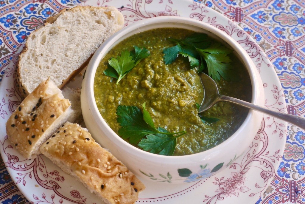A bowl of soup with a spoon and several pieces of bread on a white plate with a pink border