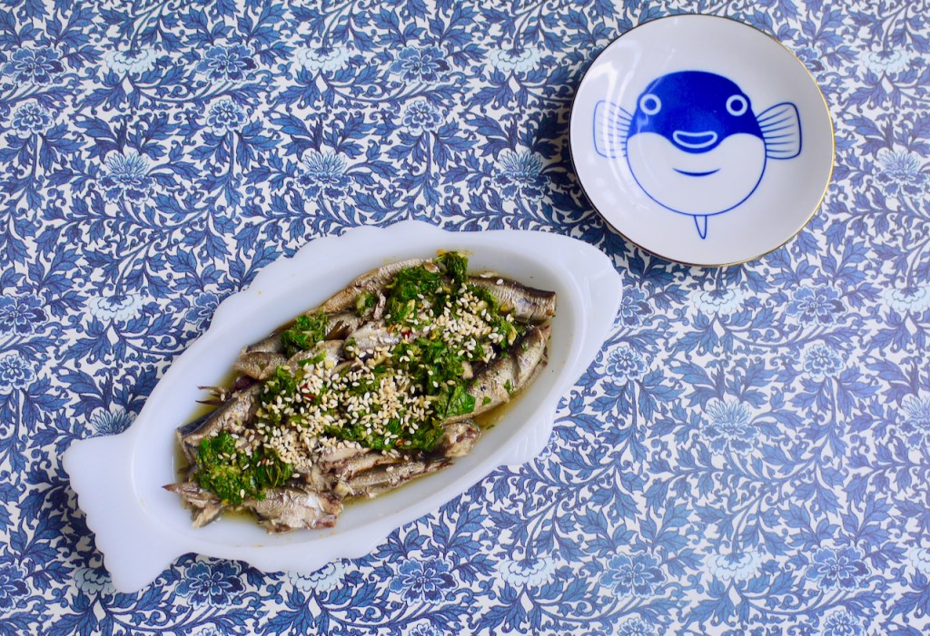 A fish-shaped dish of sardines and a small round plate with a fish on it, on a blue patterned background