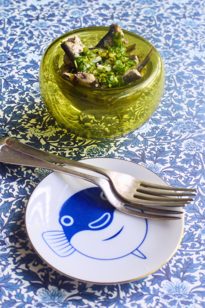 A green glass bowl of sardines, a small round plate with a fish on it, and two forks