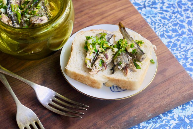A piece of bread with sardines and parsley on it, and two forks