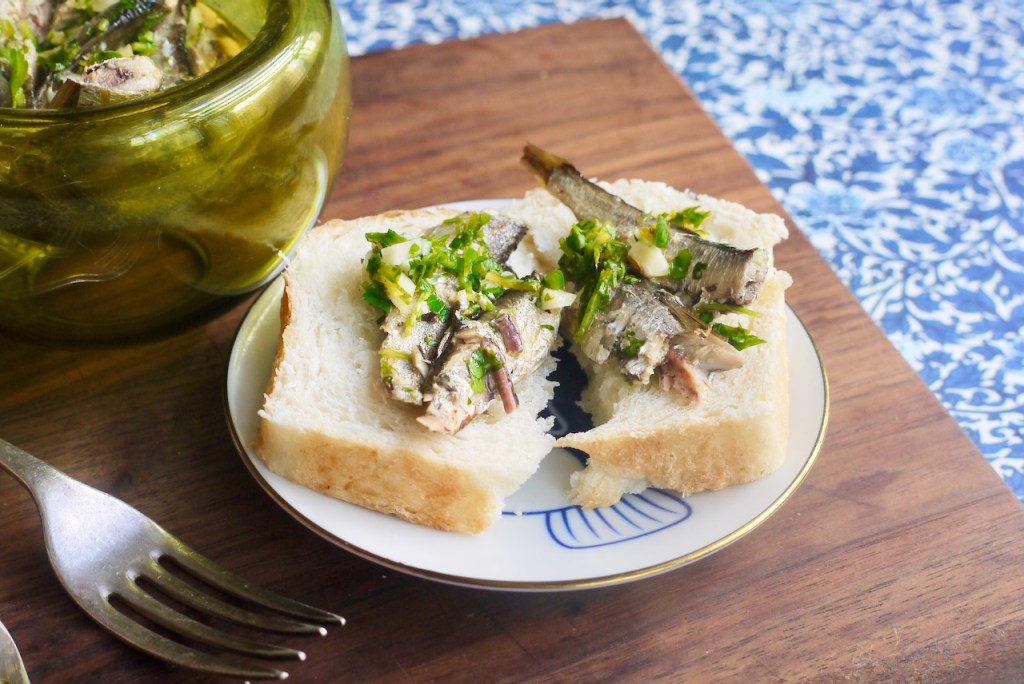 A torn piece of bread with sardines and parsley on it