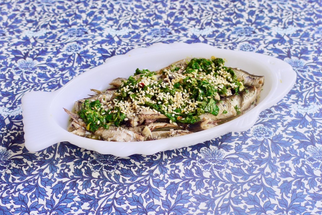 A white fish-shaped dish of sardines on a blue patterned background
