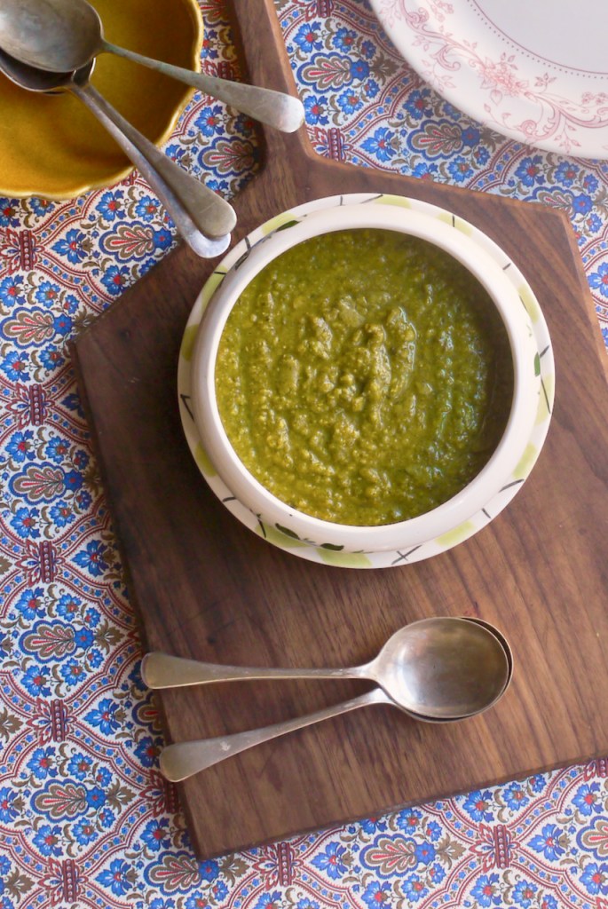 Green soup on a wooden board with two spoons and plates in the background.jpeg